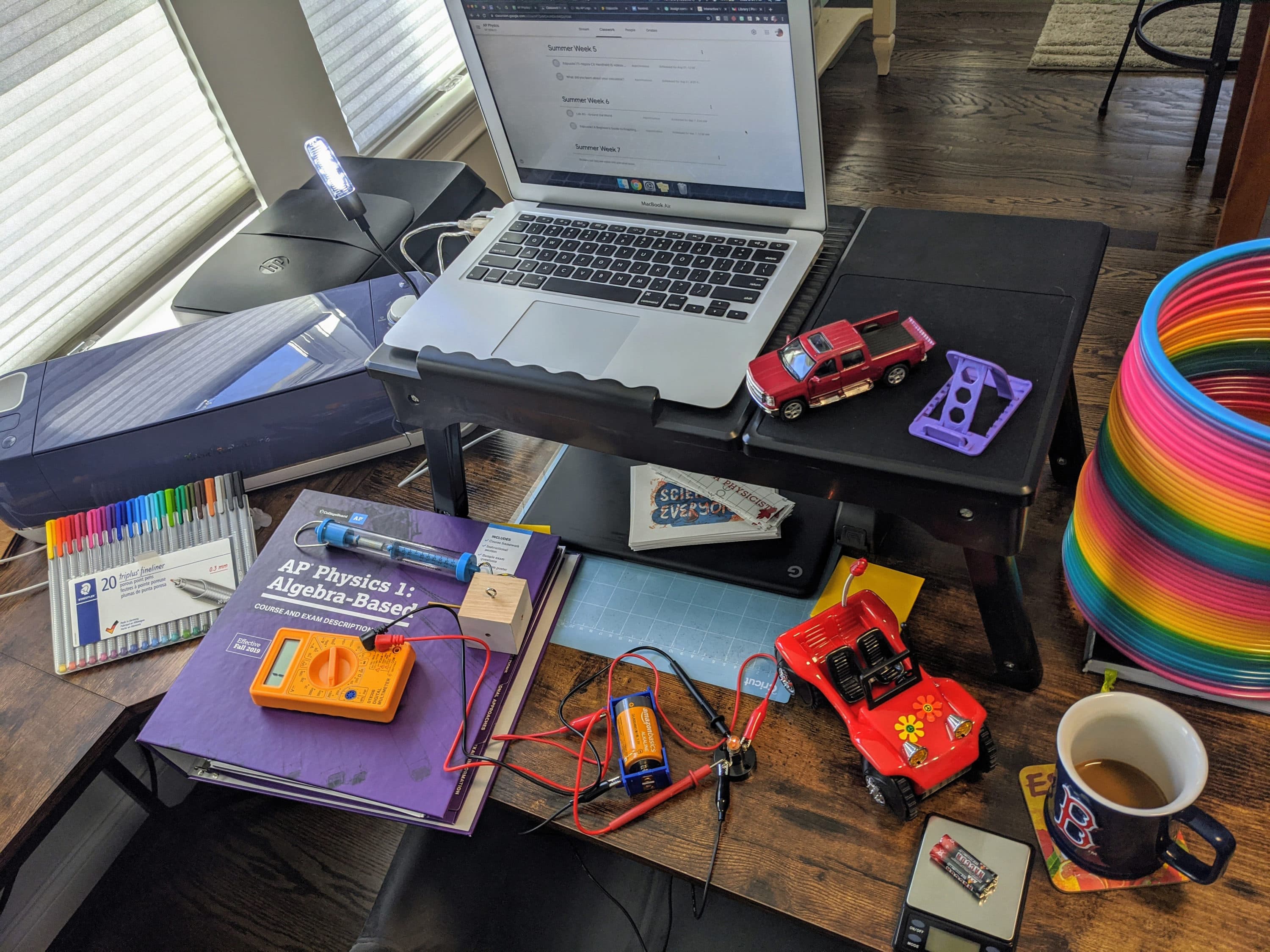 A laptop, various remote-control cars and other physics-friendly objects on a desk.
