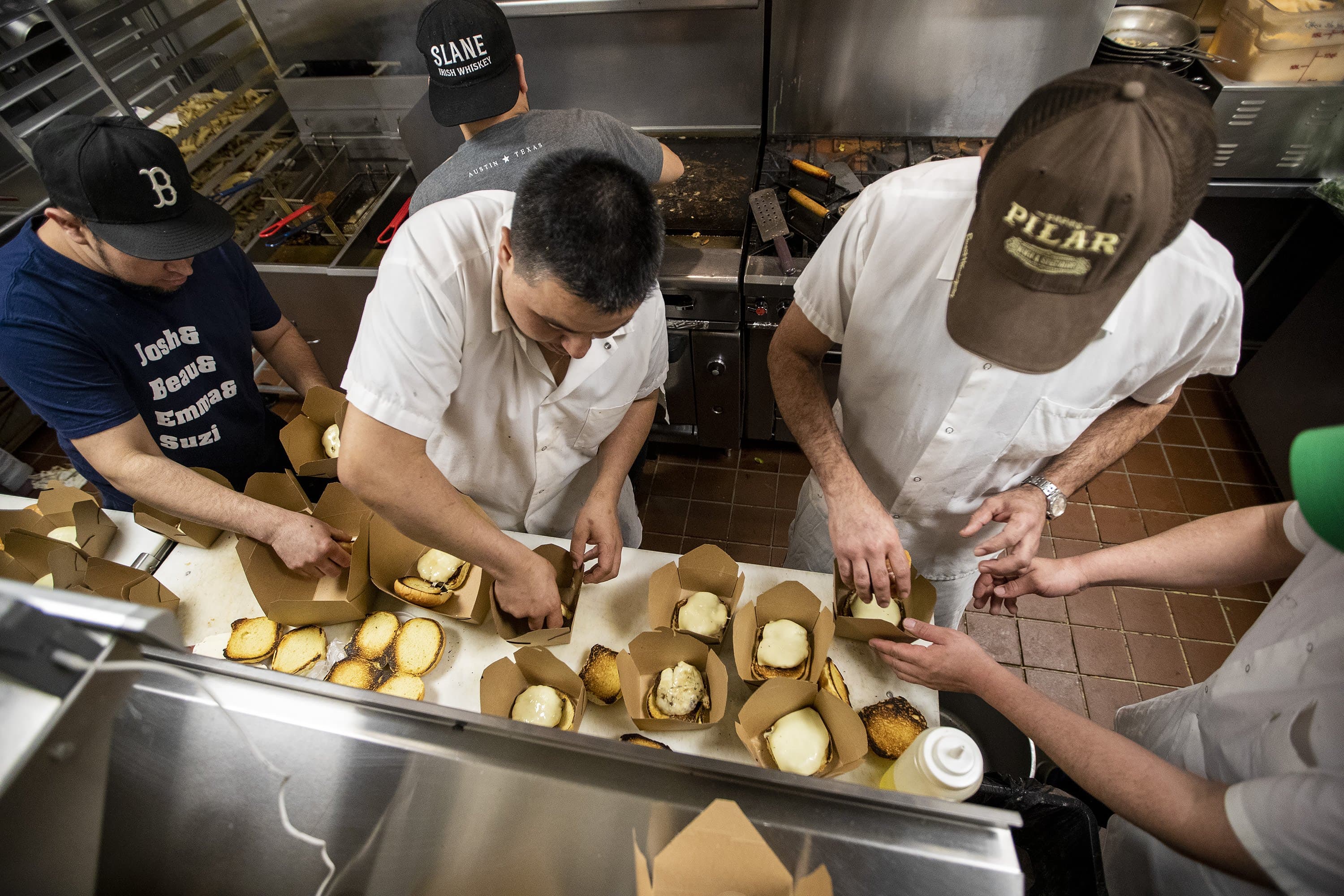March 16: Baker closes all public and private schools until April 6, and bans eating inside bars and restaurants. He also puts a ban on gatherings of over 25 people. Pictured here, the kitchen staff at Trina’s Starlite Lounge in Somerville assembling hamburgers and cheeseburgers. All the food prepared was made with food the restaurant would have discarded due to the state's order beginning March 17, preventing people from gathering at bars and restaurants, a move to reduce the risk of spreading the coronavirus. All the proceeds of the sales went to their staff. (Jesse Costa/WBUR)