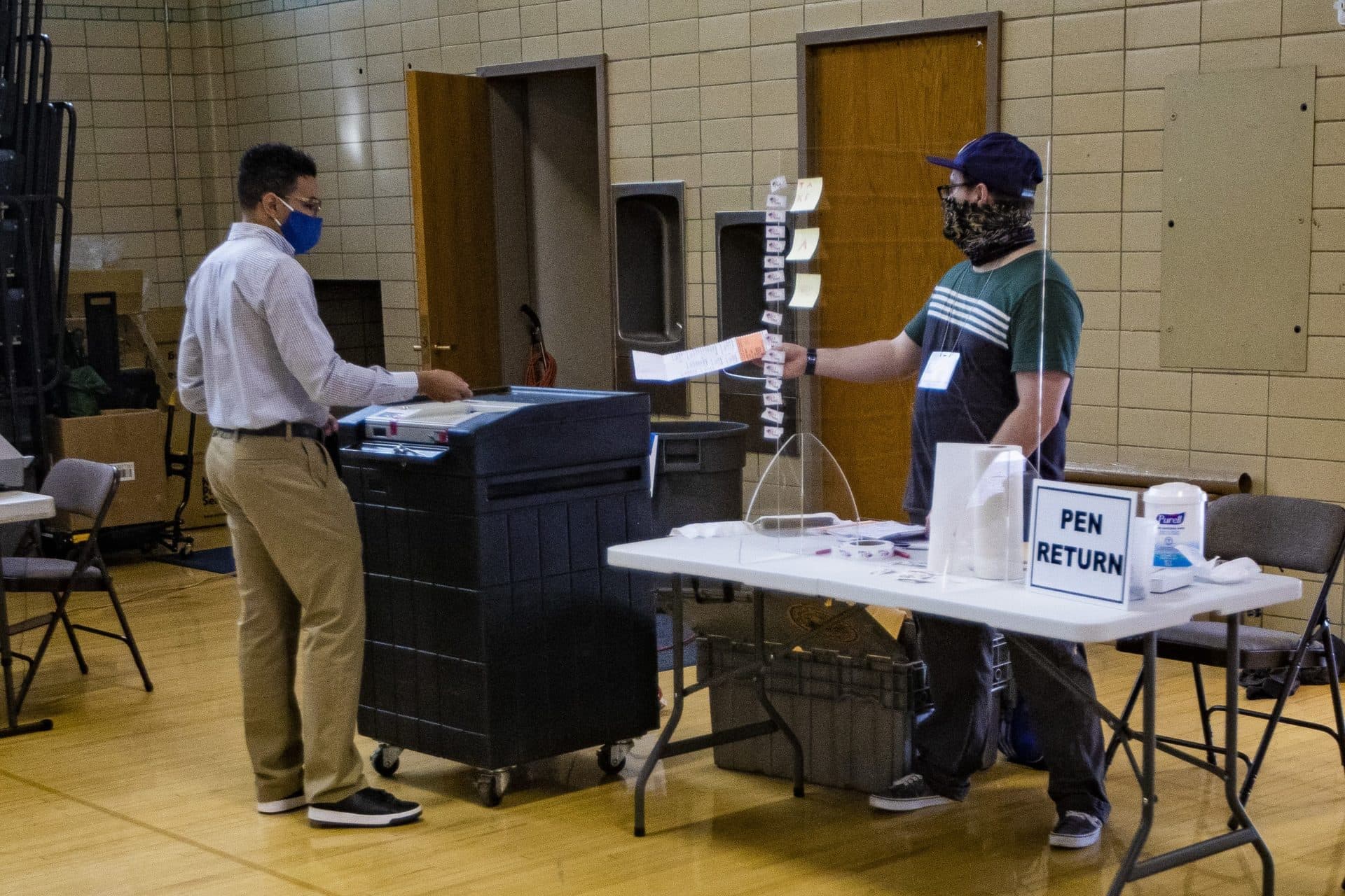 Election workers at the Brookline High School enter early voting ballots for precinct 6 into a ballot machine. (Jesse Costa/WBUR)