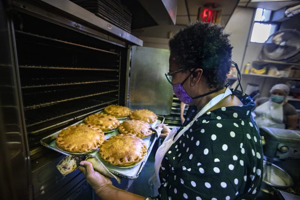 Petsi Pies founder and owner Renee McLeod pulls out and inspects a pan of apple pies baking in the oven. (Jesse Costa/WBUR)
