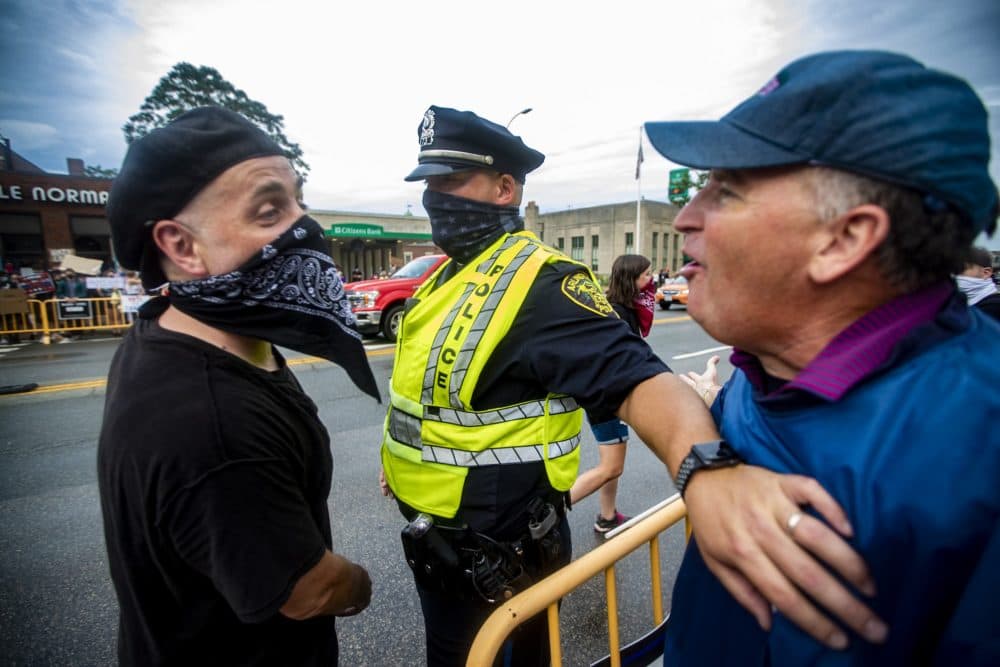 An Arlington police officer holds back a Back the Blue supporter having words with a Black Lives Matter counter-protester during opposing rallies held in front of Arlington City Hall. (Jesse Costa/WBUR)