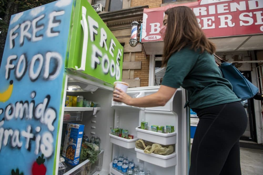 Local resident Jessica Ernst places a container of tomato sauce, which she made in her kitchen at home, into the community refrigerator. (Jesse Costa/WBUR)