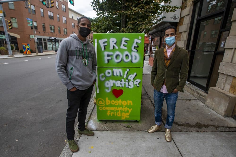 Josiel Gonzalez, left, and Haithem Abdella stand in front of the community refrigerator. (Jesse Costa/WBUR)