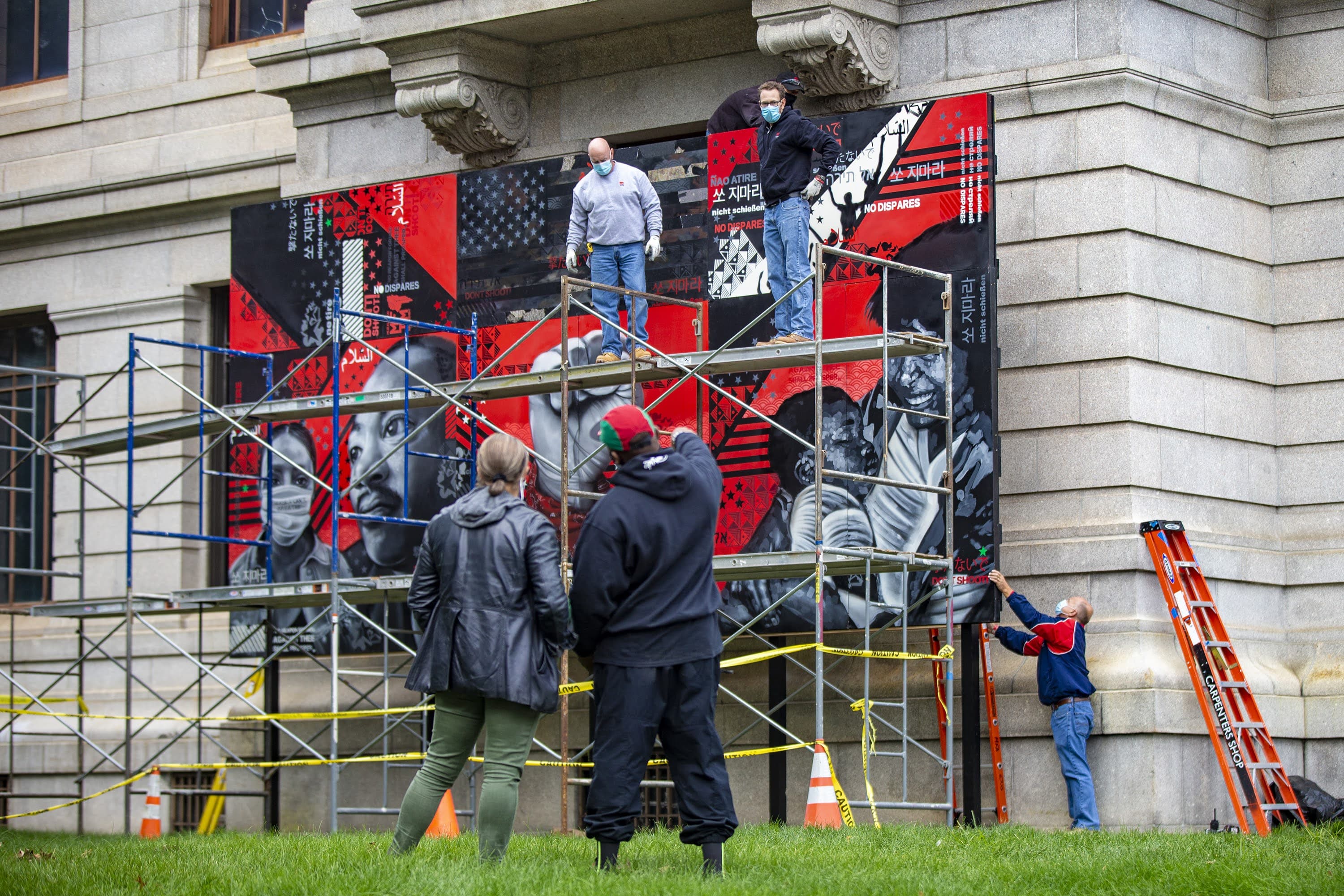 Museum of Fine Arts’ Makeeba McCreary and artist Problak Gibbs oversee the installation “No Weapon Formed Against Thee Shall Prosper” created by Cey Adams, Sophia Dawson and Victor “Marka27” Quiñonez on the museum’s Huntington Avenue lawn. (Jesse Costa/WBUR)
