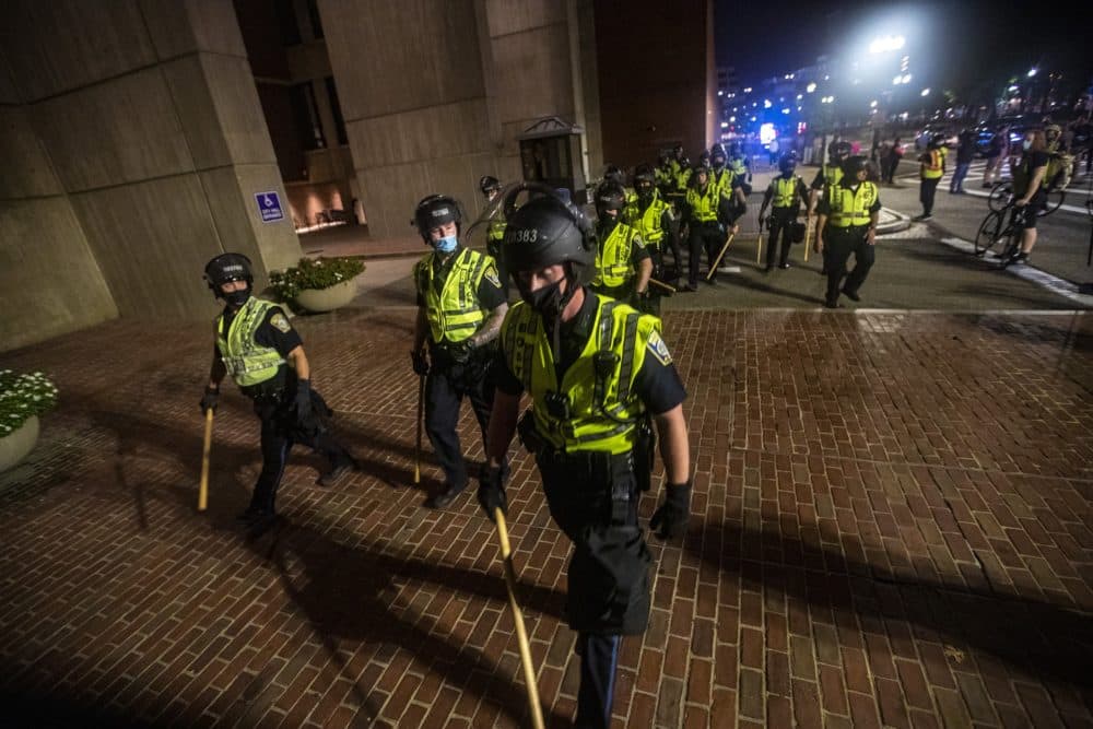 Boston Police officers armed with batons and wearing riot gear move towards the entrance of City Hall Plaza as protesters gather on Congress Street during the Justice for Breonna Taylor rally. (Jesse Costa/WBUR)