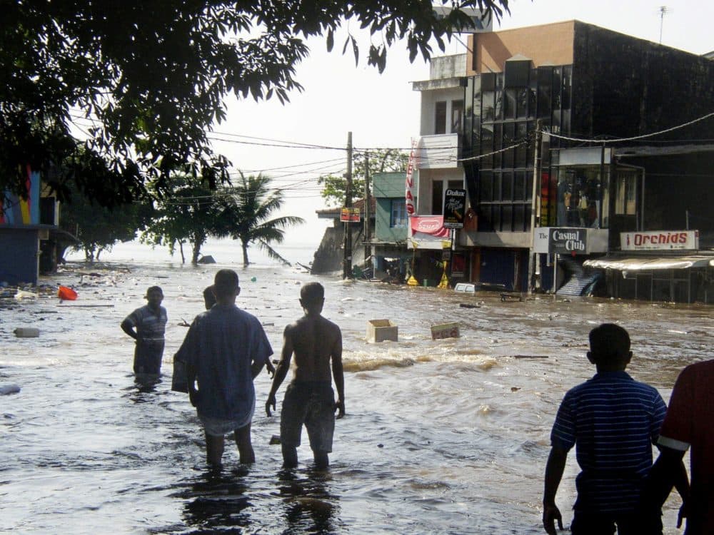 In this picture taken 26 December 2004, Sri Lankan pedestrians walk through floodwaters in a main street of Galle, after the coastal town was hit by a tidal wave. (STR/AFP via Getty Images)