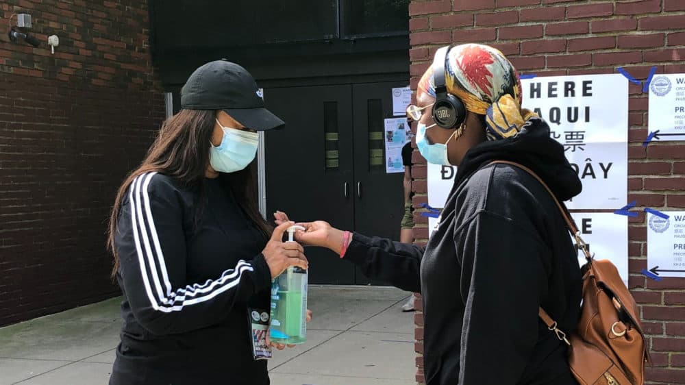 Elections inspector Danita Underwood offers voters hand sanitizer on their way into vote at the Shelburne Community Center in Roxbury. (Shannon Dooling/WBUR)