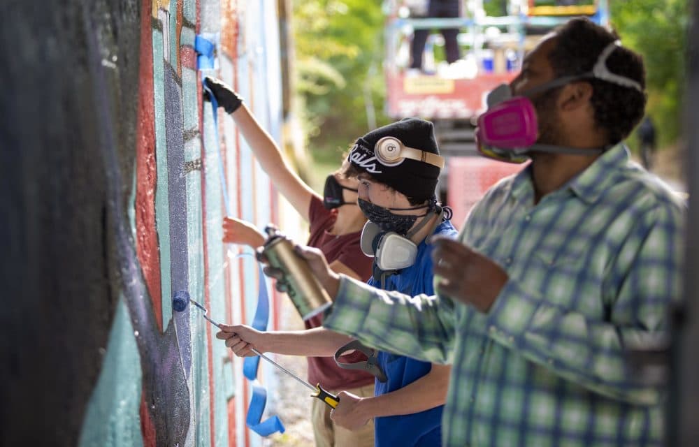 Student artist Brennan Commisso, center, works on a cityscape and ocean wildlife mural on the East Boston Greenway with Jason Talbot and Delila Montañez. (Robin Lubbock/WBUR)