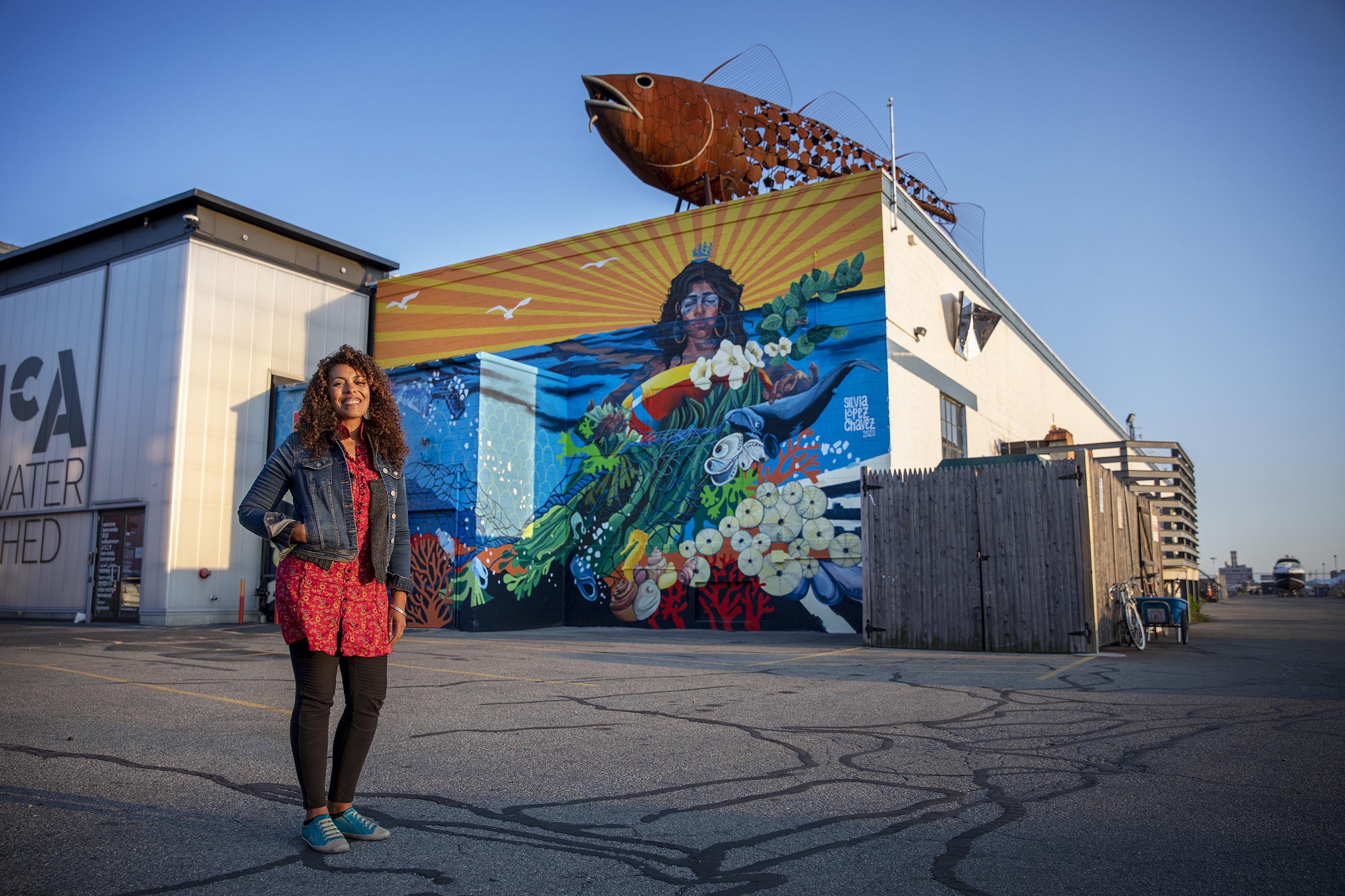 Artist Silvia López Chavez by her mural "Rise" at the Boston Harbor Shipyard and Marina in East Boston. (Robin Lubbock/WBUR)