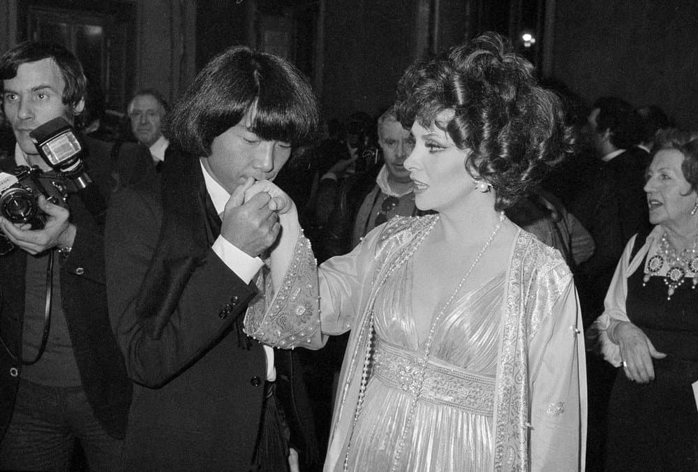 In this Dec. 16, 1977 file photo, designer Kenzo Takada kisses the hand of Italian actress Gina Lollobrigida after she awarded him as one of the ten most elegant men in the world in Rome, Italy. Fashion designer Kenzo Takada dies from COVID-19 complications at age 81 near Paris, spokeswoman and reports said Sunday Oct. 4, 2020. (AP)