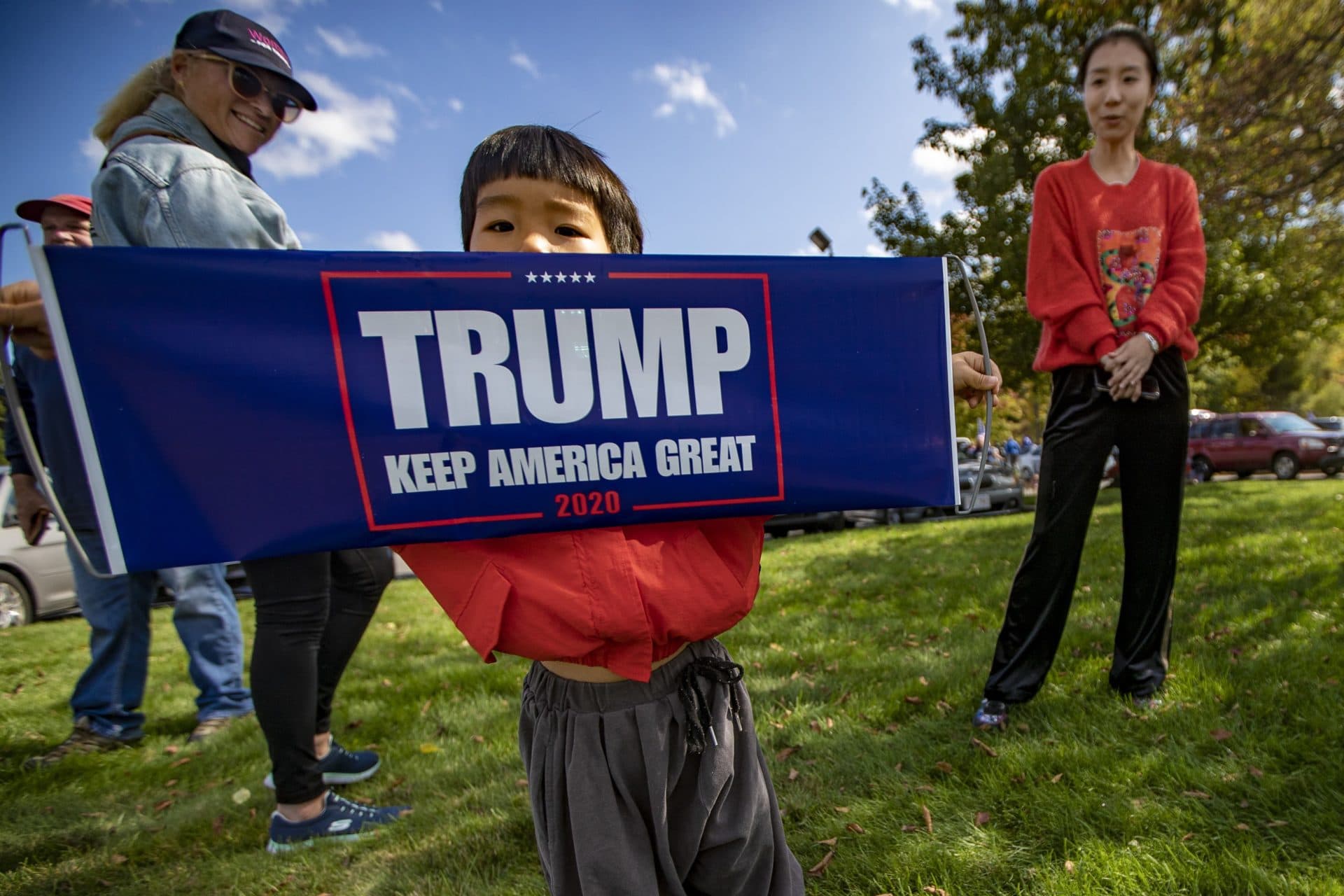 Three-year-old Lucas Wang holds a Trump banner at the Lexington Service Center on Route 95 during the Trump Train caravan. (Jesse Costa/WBUR)