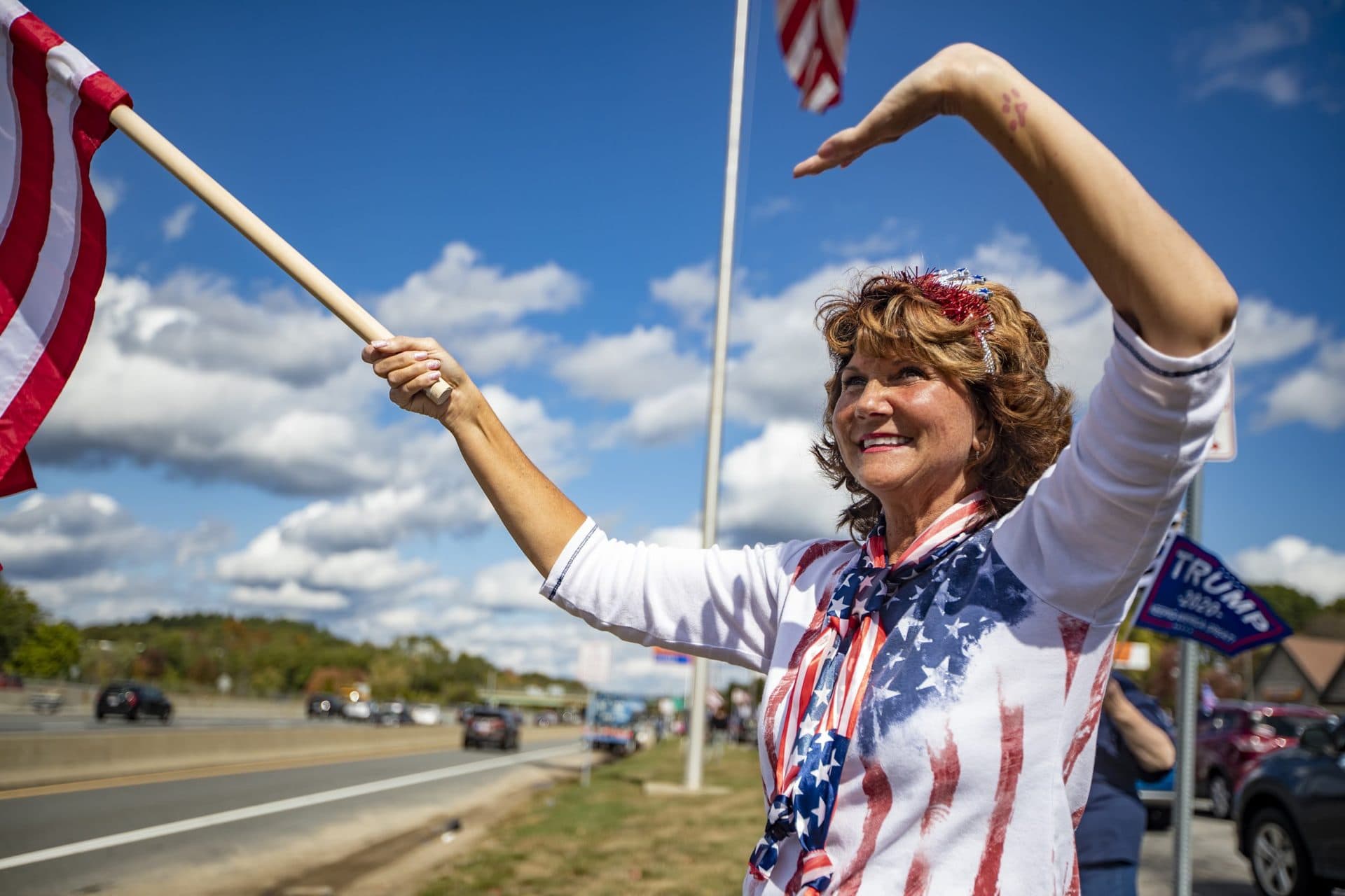 Grace Lincoln holds a flag and waves to passing driver on 95 at the Lexington Serve Center during the Trump Train caravan. (Jesse Costa/WBUR)