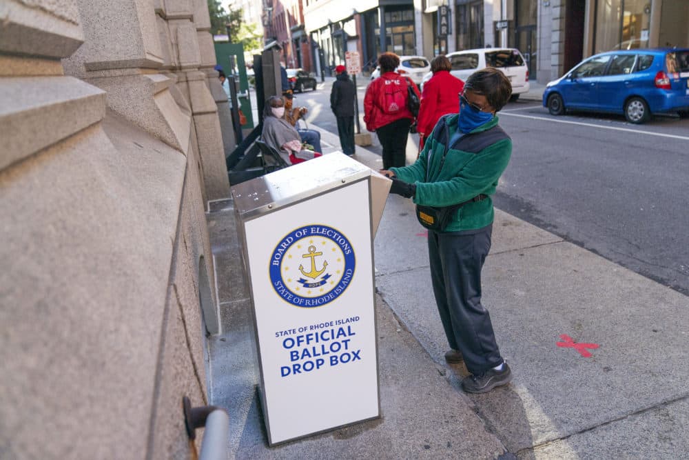 In this Oct. 14 photo, Eva Abodoadji drops off a mail ballot into an official ballot drop box as voters wait in line at City Hall as in-person early voting begins for the general election in Rhode Island in Providence. (David Goldman/AP)
