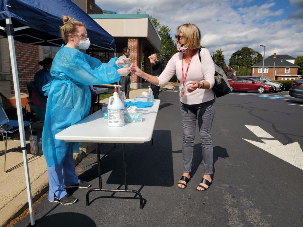 Nurse Michelle Laracy hands Watertown schools staff member Maureen Craig a swab for a coronavirus test outside Watertown Middle School. (Angus Chen for WBUR)