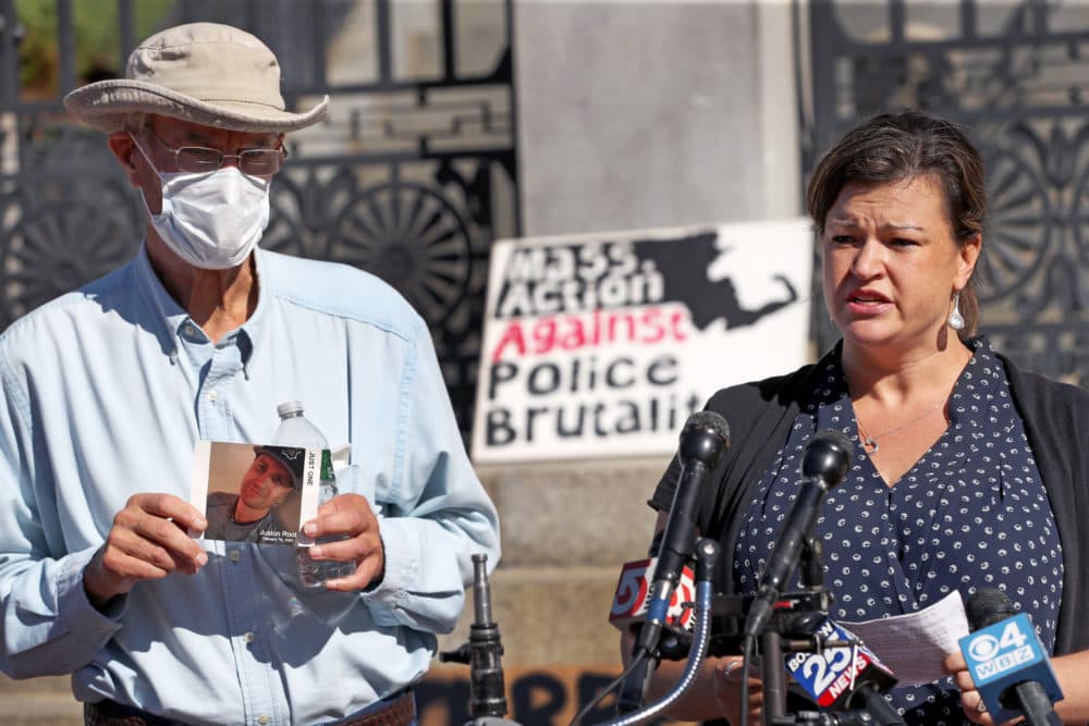 On the steps of the Massachusetts State House in Boston, Jennifer Root Bannon speaks at the podium on Sept. 4. Juston's father Evan Root holds a photograph of his son. Also in attendance were Mass Action Against Police Brutality and families of loved ones lost to police violence. (David L. Ryan/The Boston Globe via Getty Images)