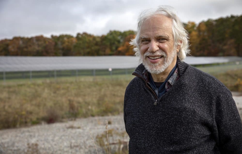 Gerry Palano, an alternative energy specialist at the Massachusetts Department of Agricultural Resources, with and array of solar panels in a field behind him. (Robin Lubbock/WBUR)