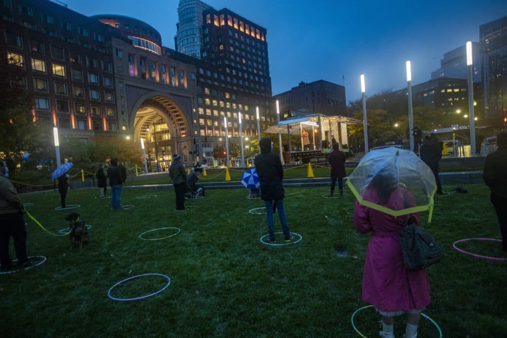 The audience, standing and sitting in hula hoops six-feet apart, watch the performance in the drizzling rain. (Jesse Costa/WBUR)