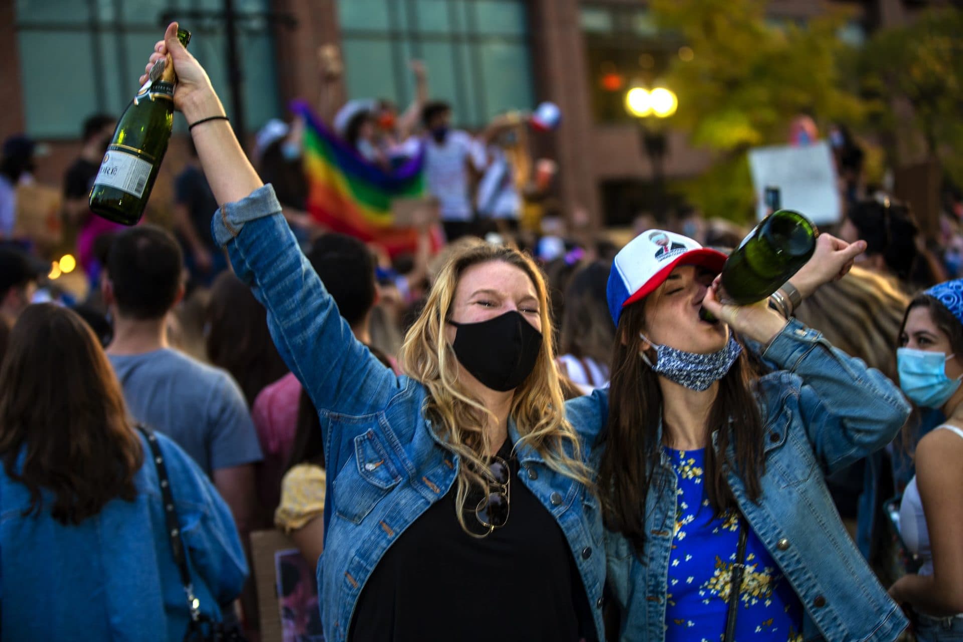 Two women celebrate Joe Biden’s presidential victory drinking bottles of champagne on Boylston Street. (Jesse Costa/WBUR)