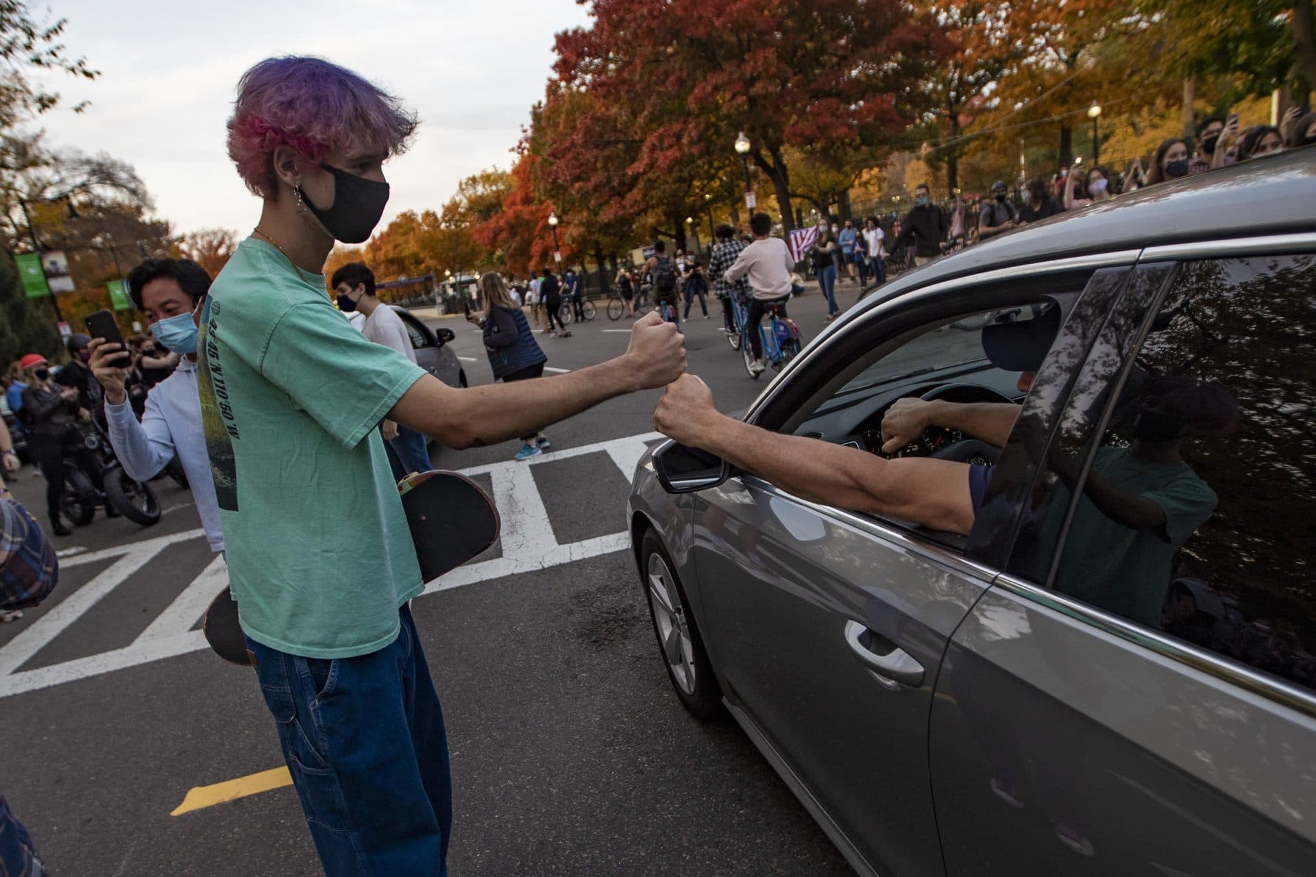 A man in a passing car and a skateboarder fist bump to celebrate Joe Biden’s presidential victory on Charles Street. (Jesse Costa/WBUR)