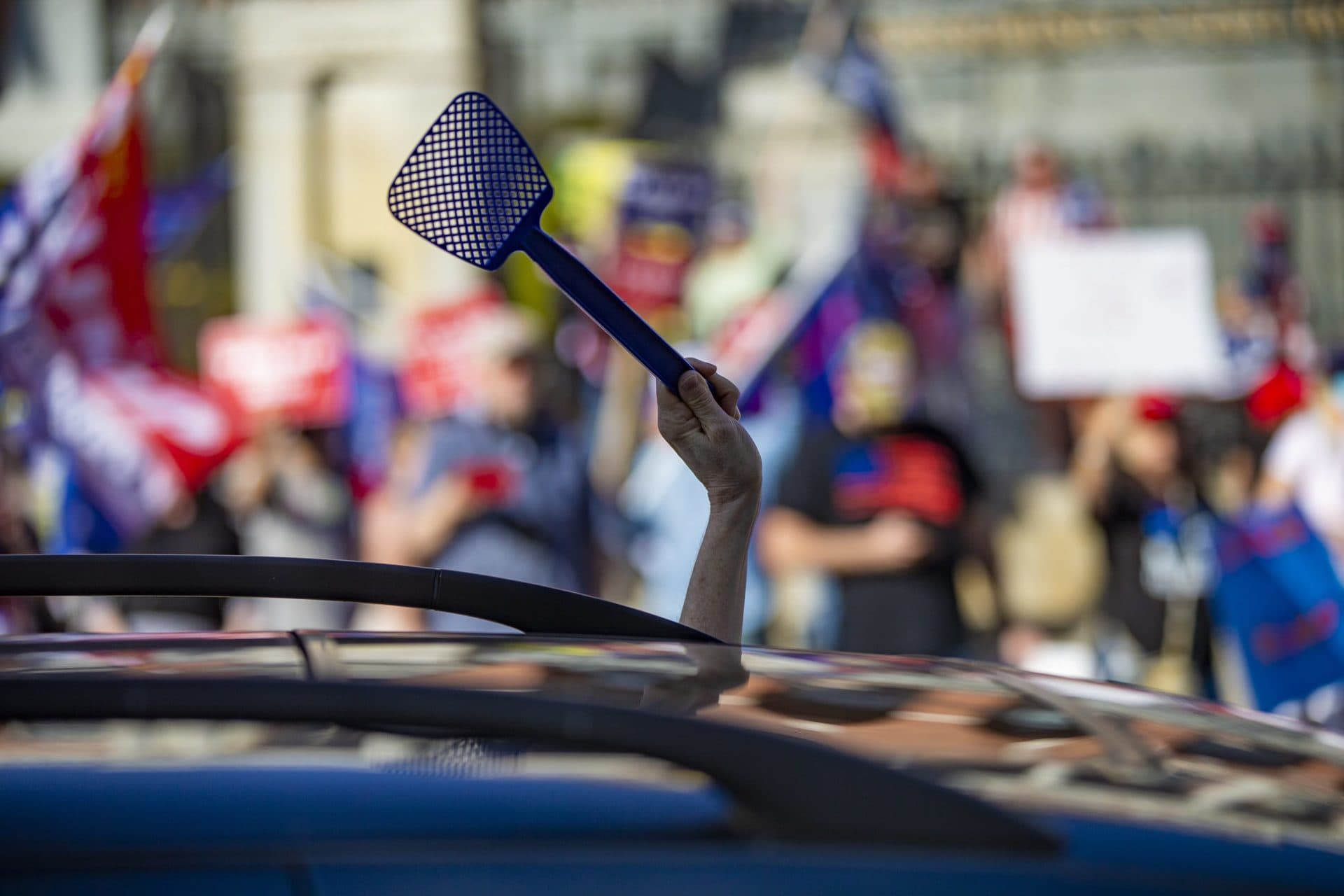 A Biden supporter waves a fly swatter at a Trump rally in front of the Massachusetts State House. (Jesse Costa/WBUR)