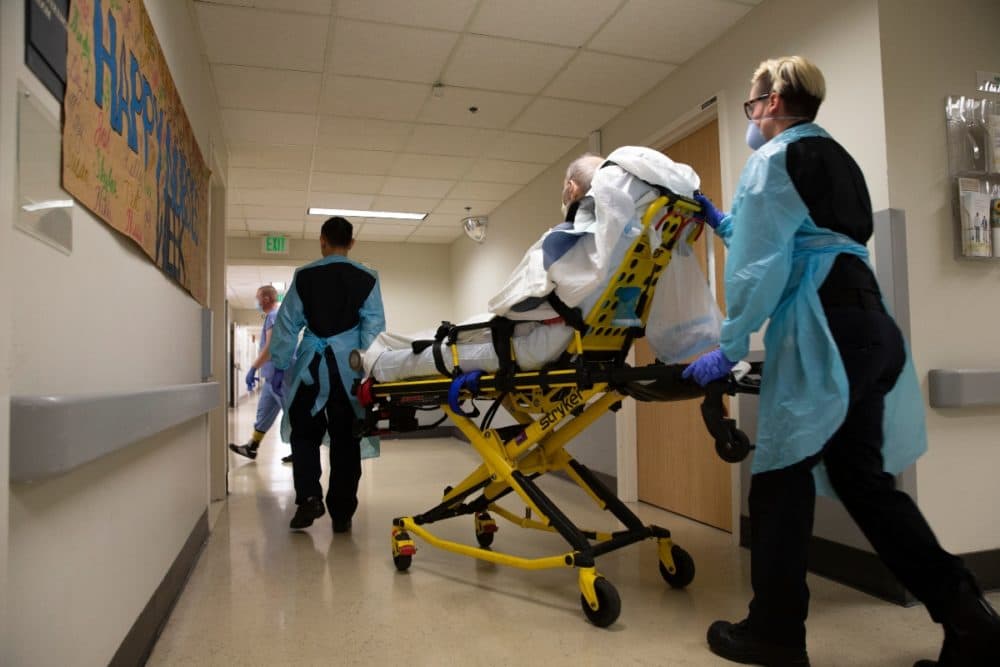 An EMT transfers a patient out of an acute care COVID unit at Harborview Medical Center in Seattle in May. As a second surge begins in Massachusetts, hospitals are planning to pool resources to manage an increase in patients. (Karen Ducey/Getty Images)