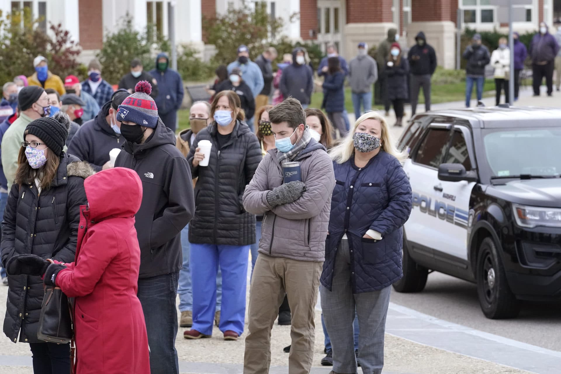 Voters wait in line near a police vehicle outside a polling station at Marshfield High School. (Steven Senne/AP)