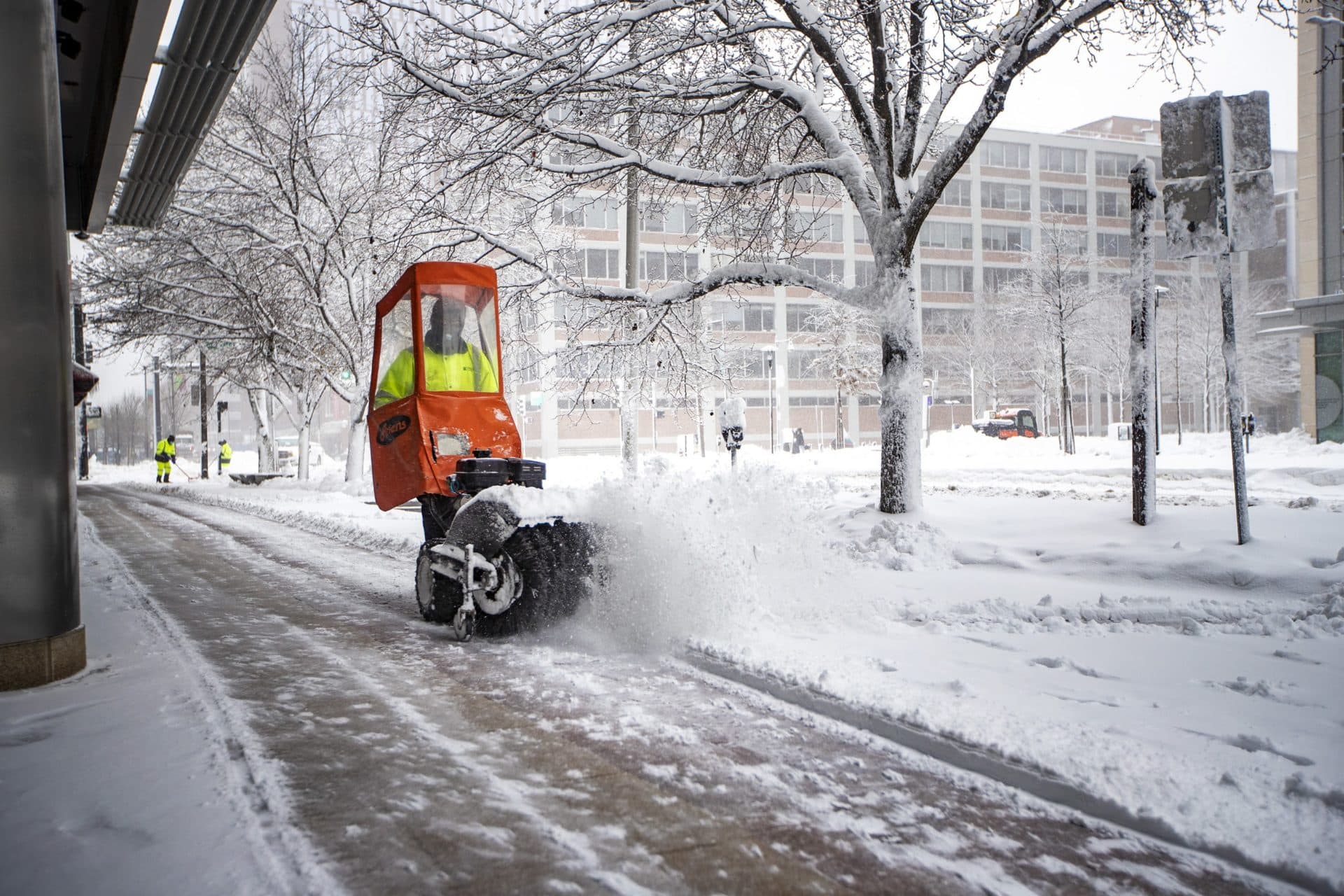 Workers clear snow from the walkway in front of the Broad Institute in Kendall Sq. (Jesse Costa/WBUR)