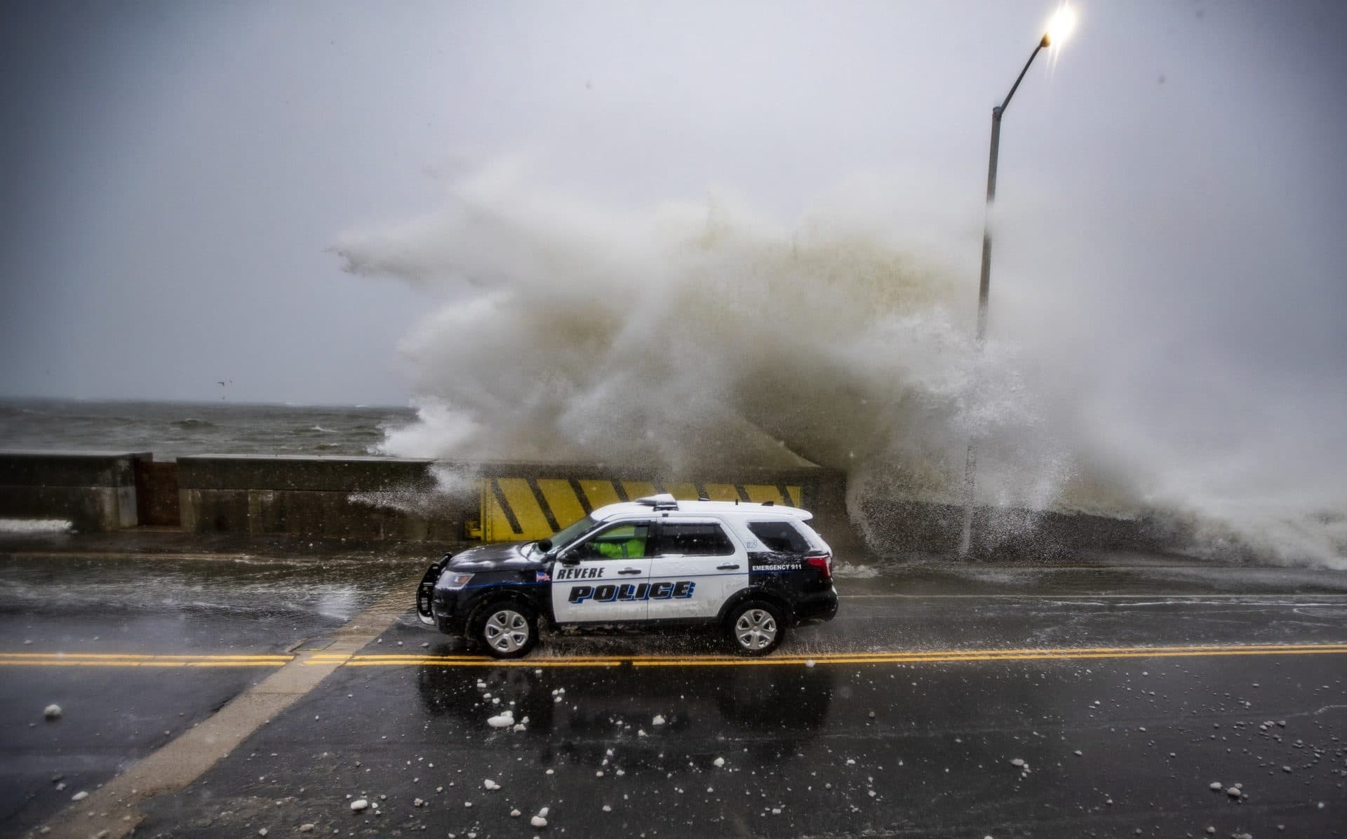 Waves crash along the seawall in Revere at high tide during the Nor’easter as a police car passes by. (Jesse Costa/WBUR)