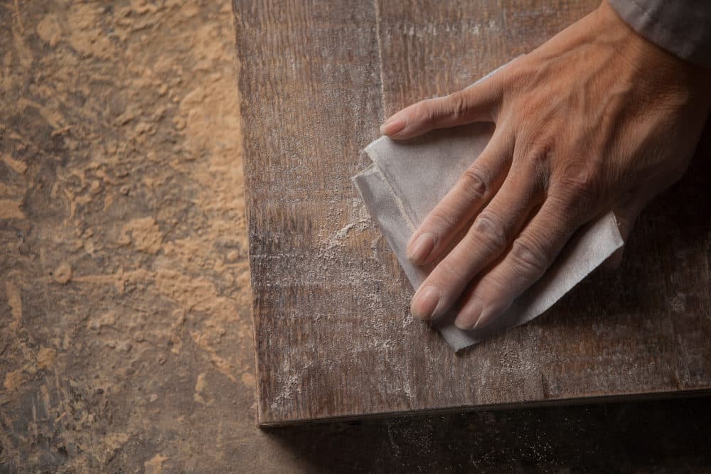 Carpenter smoothing a wood plank with sandpaper