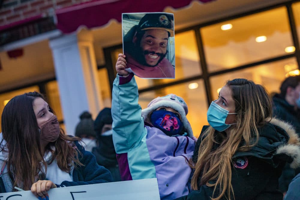 A young girl holds up a photo of Henry Tapia where hundreds of people gathered in Cushing Square in Belmont for a vigil to honor the his memory, the day after he had an altercation with a man who called him a racial slur and then drove over him, ultimately killing Tapia. (Jesse Costa/WBUR)