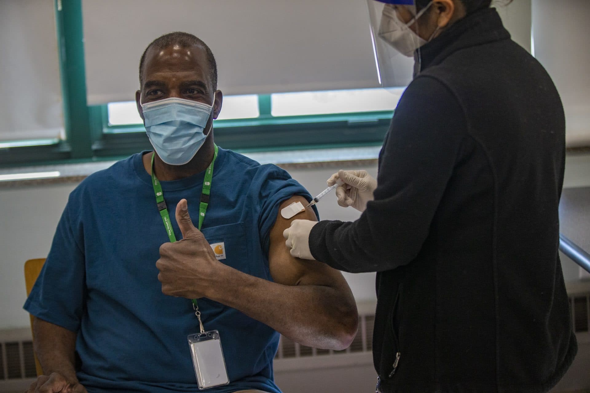 Michael Robbins, a Pine Street Inn counselor for 40 years and the organization's longest-serving employee, is the first to receive a COVID-19 vaccine at the shelter's vaccination event. Boston Health Care for the Homeless Program registered nurse Carmen Sargent is administering the shot. (Jesse Costa/WBUR)