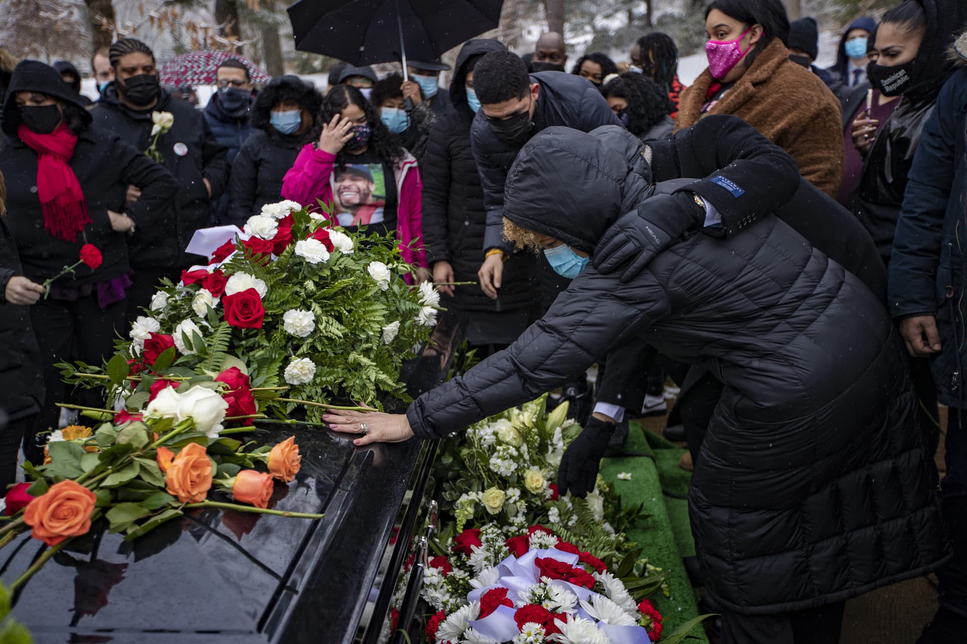 Henry Tapia’s mother Miosotis Morel places her hand onto her son’s casket at Forest Hills Cemetery. (Jesse Costa/WBUR)