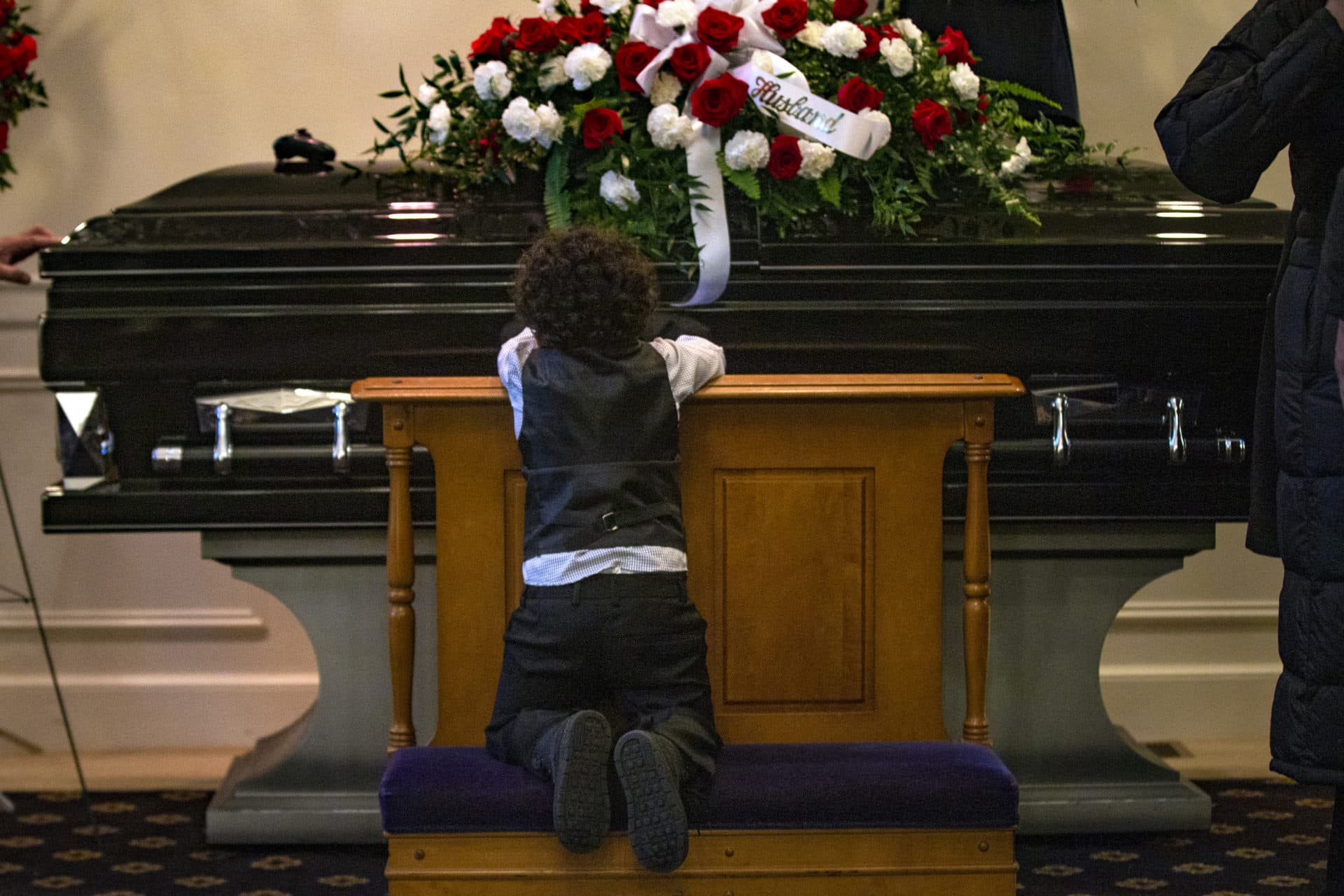 Three-year-old Eli kneels in front of his father’s casket. (Jesse Costa/WBUR)