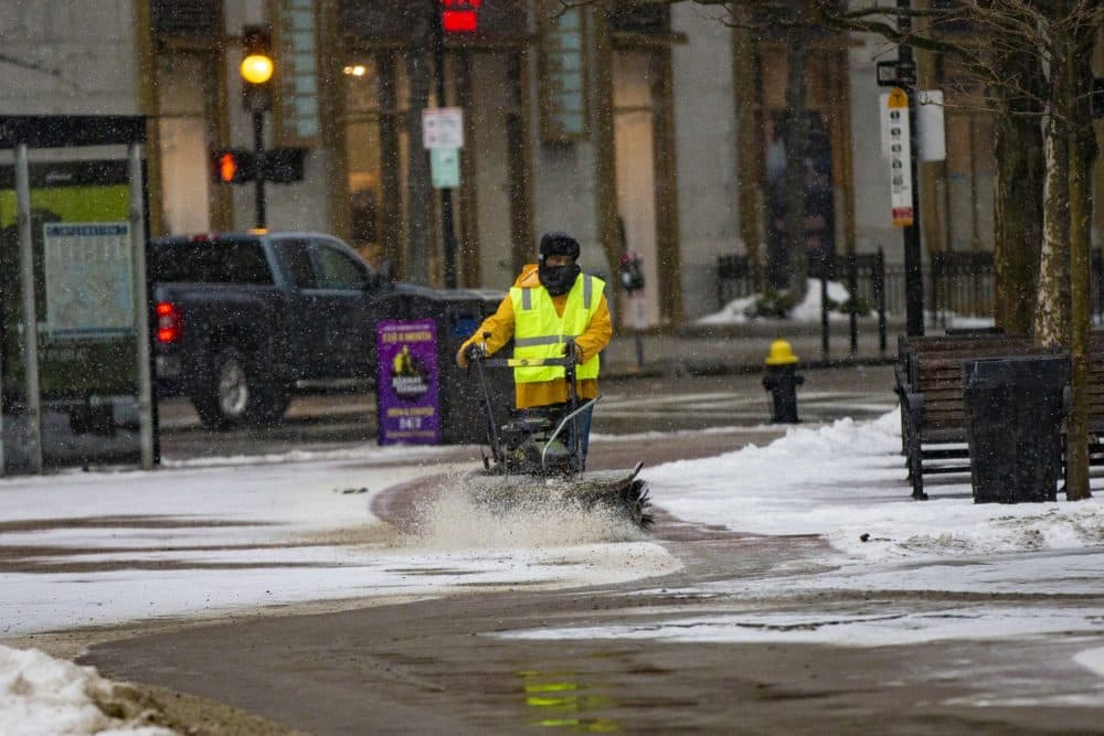 A worker clears snow from the sidewalk outside of Trinity Church in Copley Square Monday afternoon as the storm begins. (Jesse Costa/WBUR)