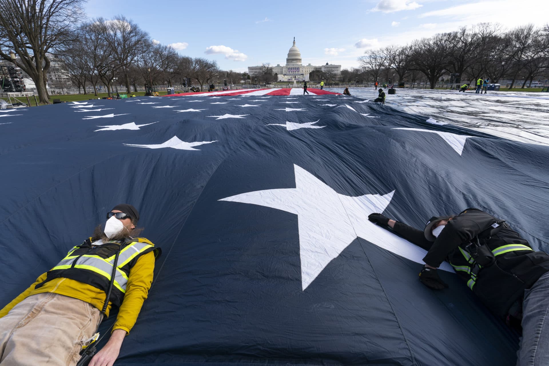 Workers use their body weight to hold down a large American flag placed on the National Mall, with the U.S. Capitol behind them. (Alex Brandon/AP)