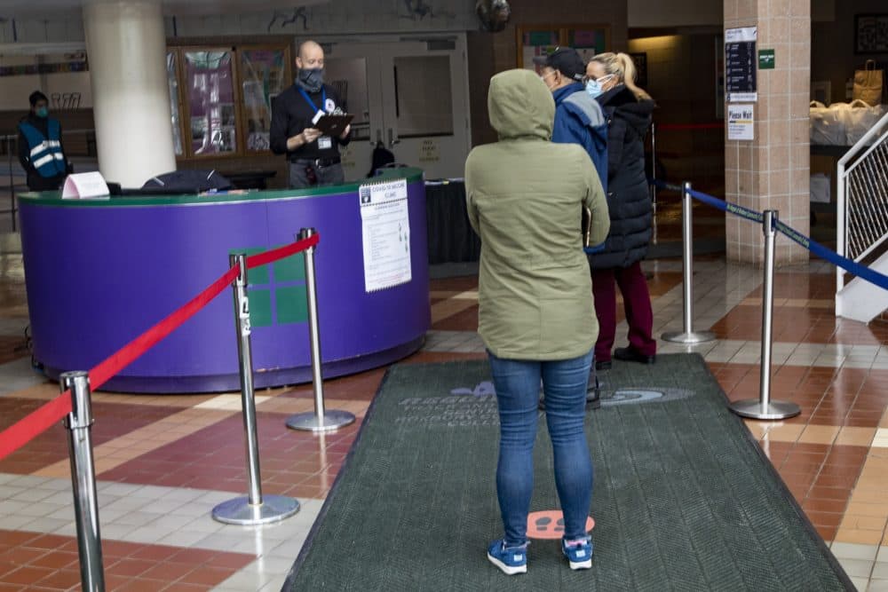 A group of people stand in line inside the Reggie Lewis Center to receive the COVID-19 vaccine. (Jesse Costa/WBUR)