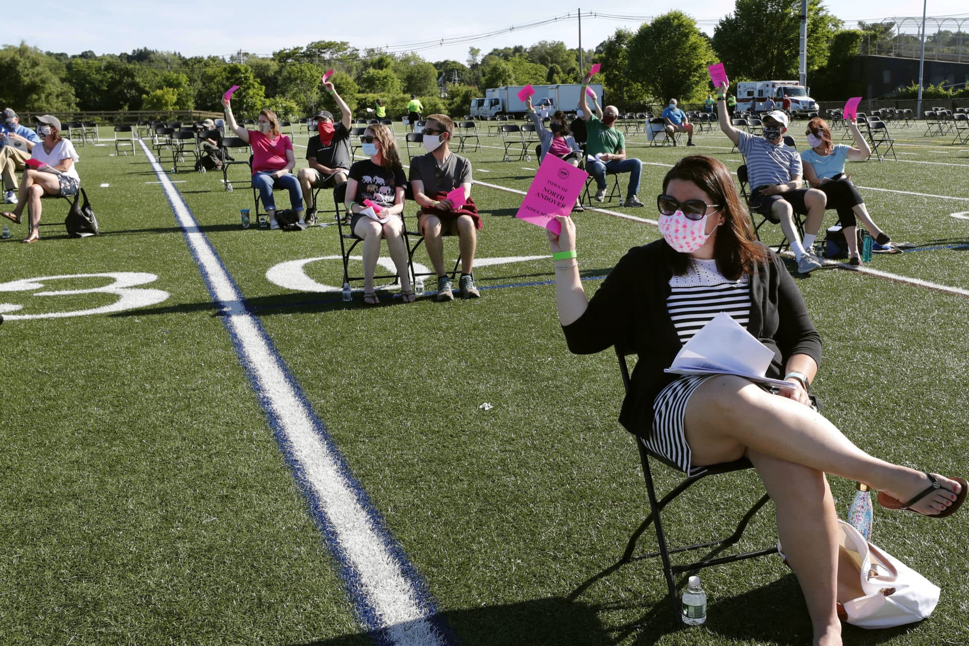 In this June 16, 2020, file photo, residents hold up pink cards to vote on an issue during the annual town meeting held at the high school football field to provide social distancing due to COVID-19 concerns, in North Andover, Mass. It was the first town meeting held outdoors since town meetings began in North Andover in 1646. (Elise Amendola/AP File)