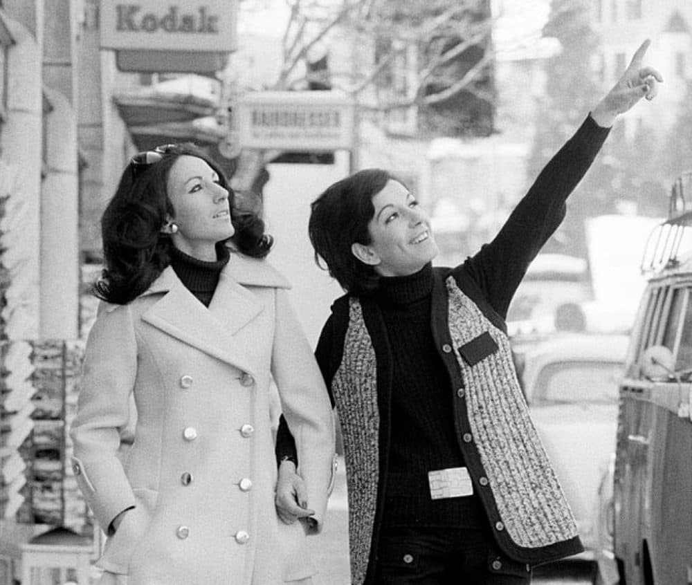 Two women walking arm in arm and watching something on the other side of the road. Sankt Moritz, March 1969 (Getty Images)