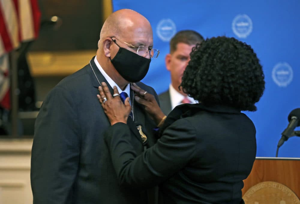 Dennis White, left, is pictured with his wife, Jackie, as she pins his new badge onto his shirt following Boston Mayor Marty Walsh, background center, swearing White in as Boston new police commissioner. (Jim Davis/Globe Staff)