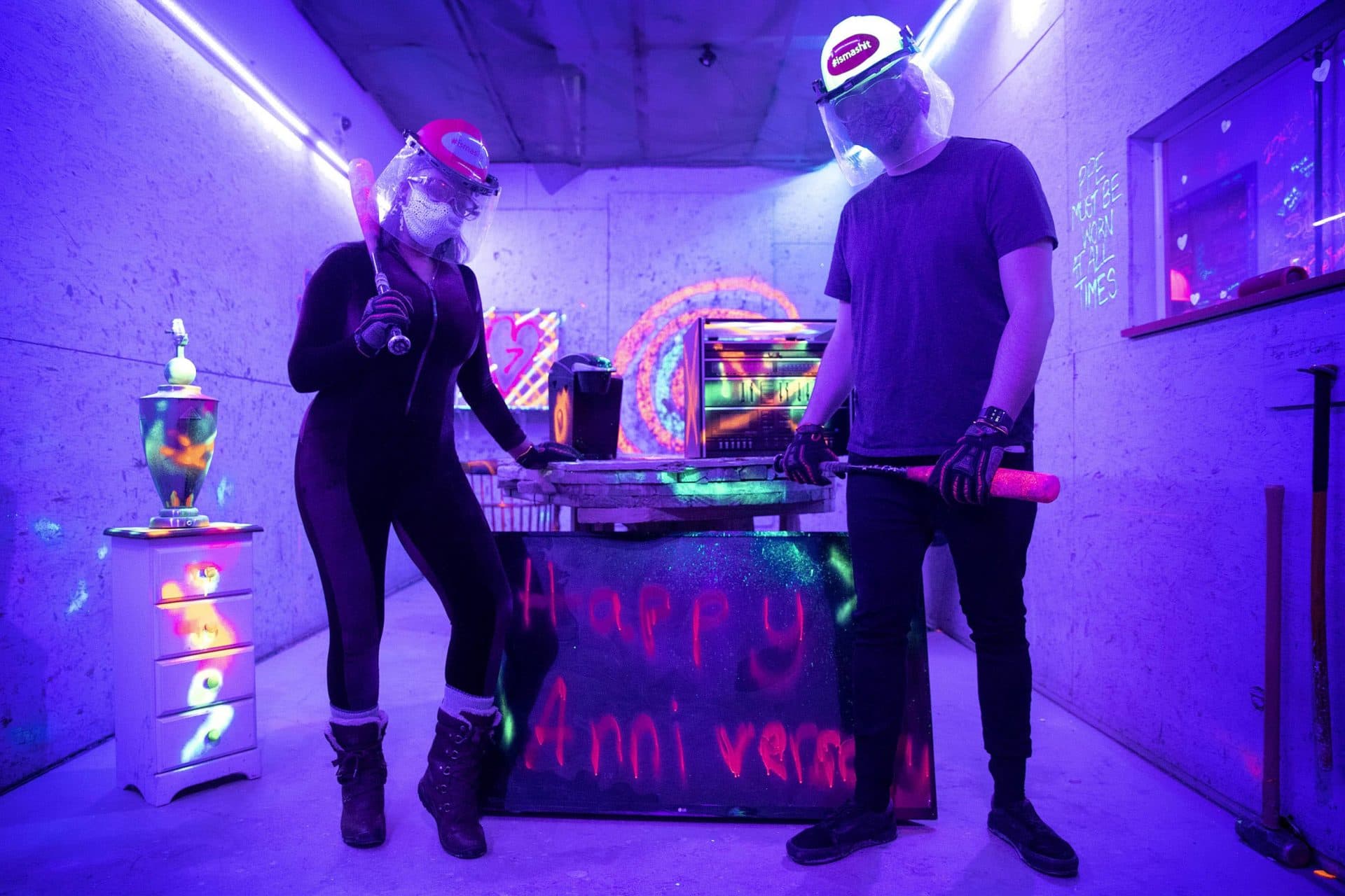 In the black light of a smash room, Kira Helper and Dmitri Burtis strike a pose before embarking on a smashing session. (Robin Lubbock/WBUR)