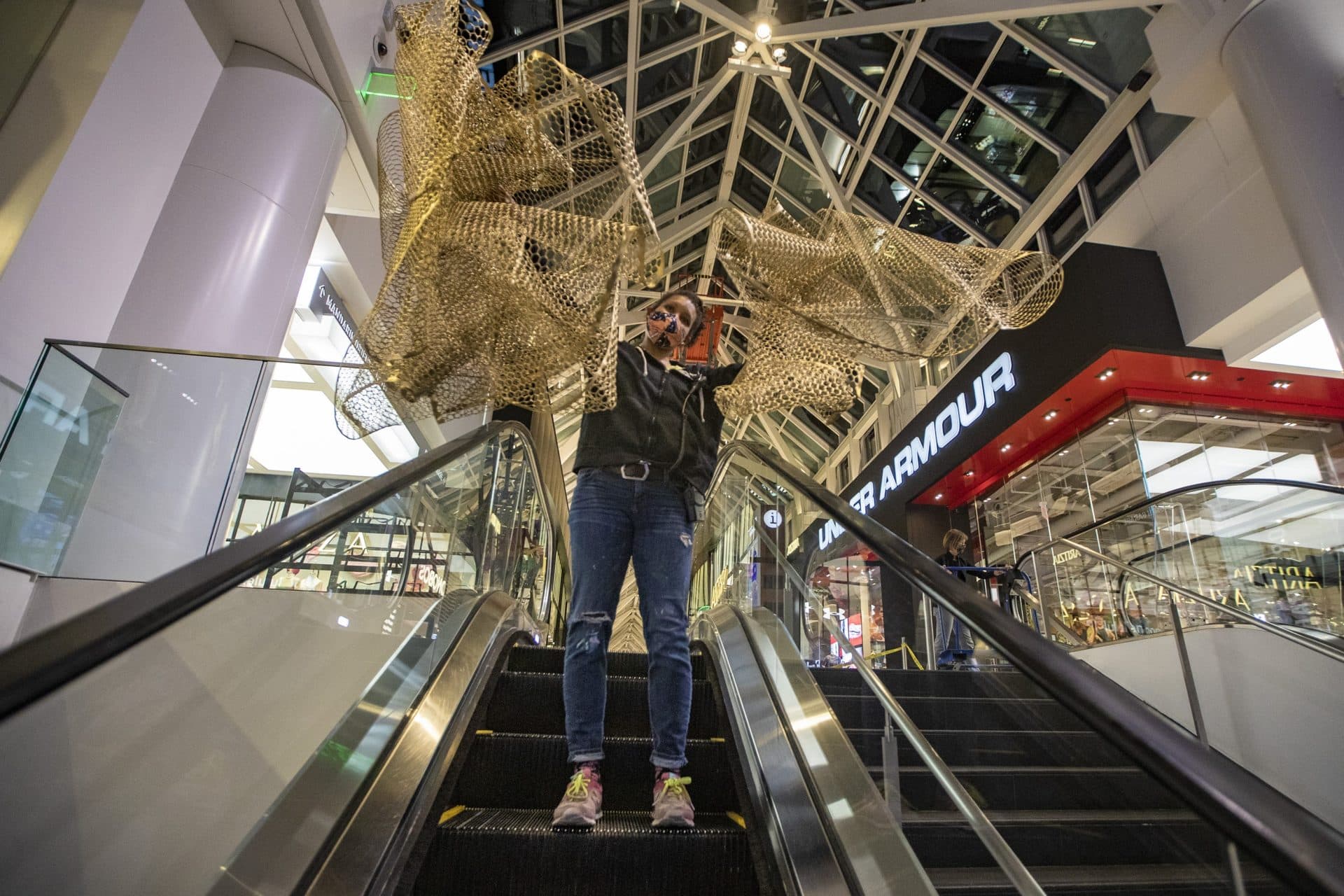 Cicely Carew rides down the escalator with two pieces of material for her “Alta Major” piece to be installed in the front entrance of the Prudential Center. (Jesse Costa/WBUR)