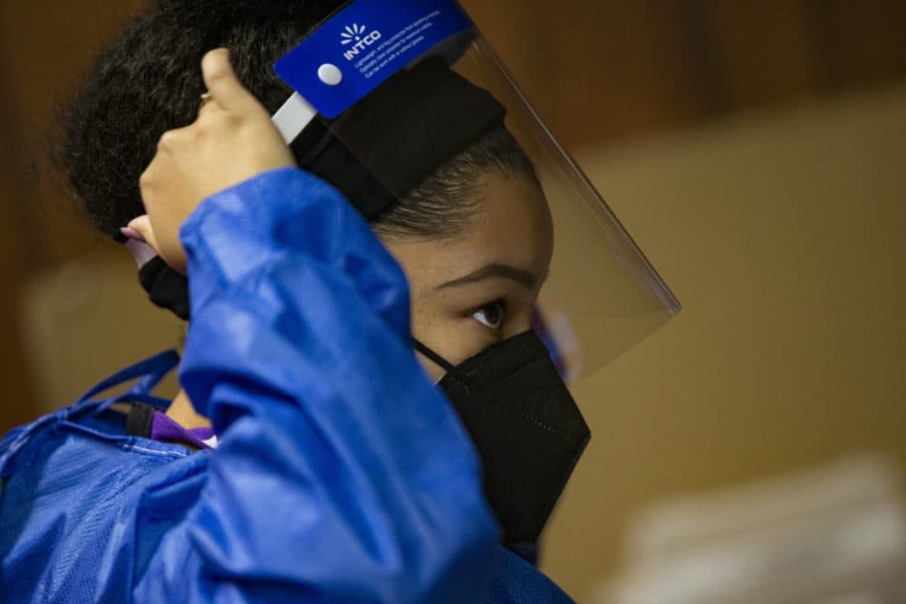 A nurse from Whittier Street Health Center puts on a face shield as she prepares to give vaccinations at the Pleasant Hill Missionary Baptist Church in Roxbury. (Jesse Costa/WBUR)