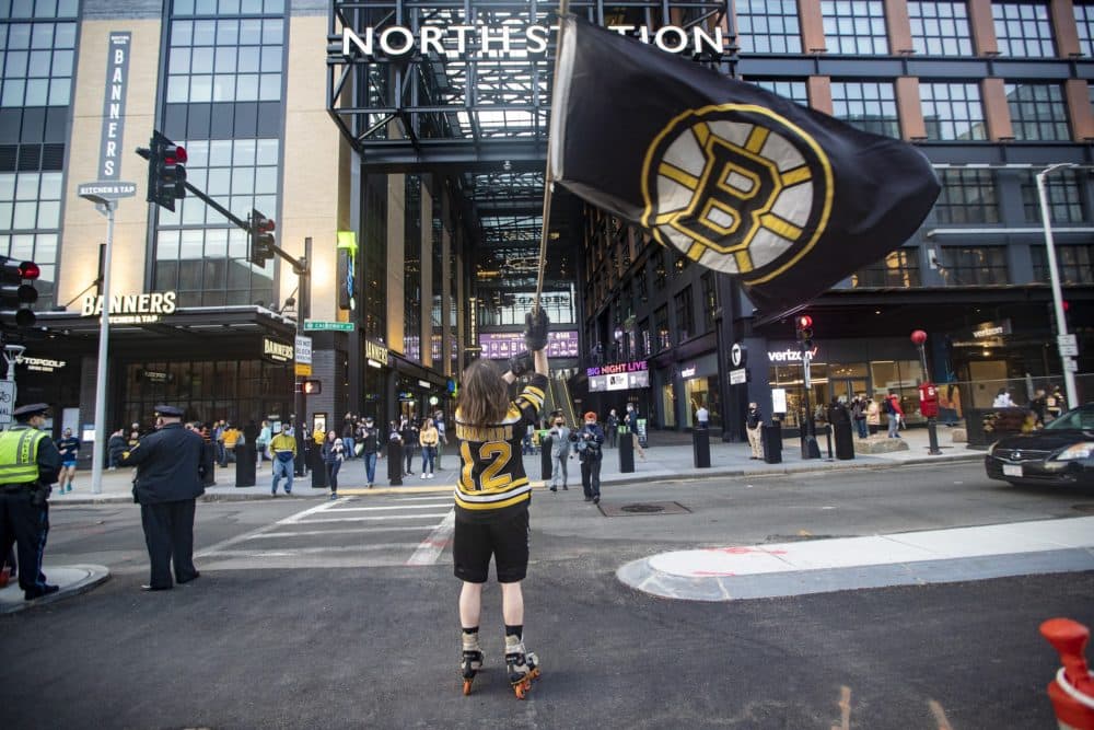 A man waves a Bruins flag on Causeway Street, in front of the entrance of TD Garden before the Bruins/Islanders game, the first game open to the public now that stadiums and arenas are permitted to hold up to 12% capacity since they were restricted by COVID-19 protocols. (Jesse Costa/WBUR)