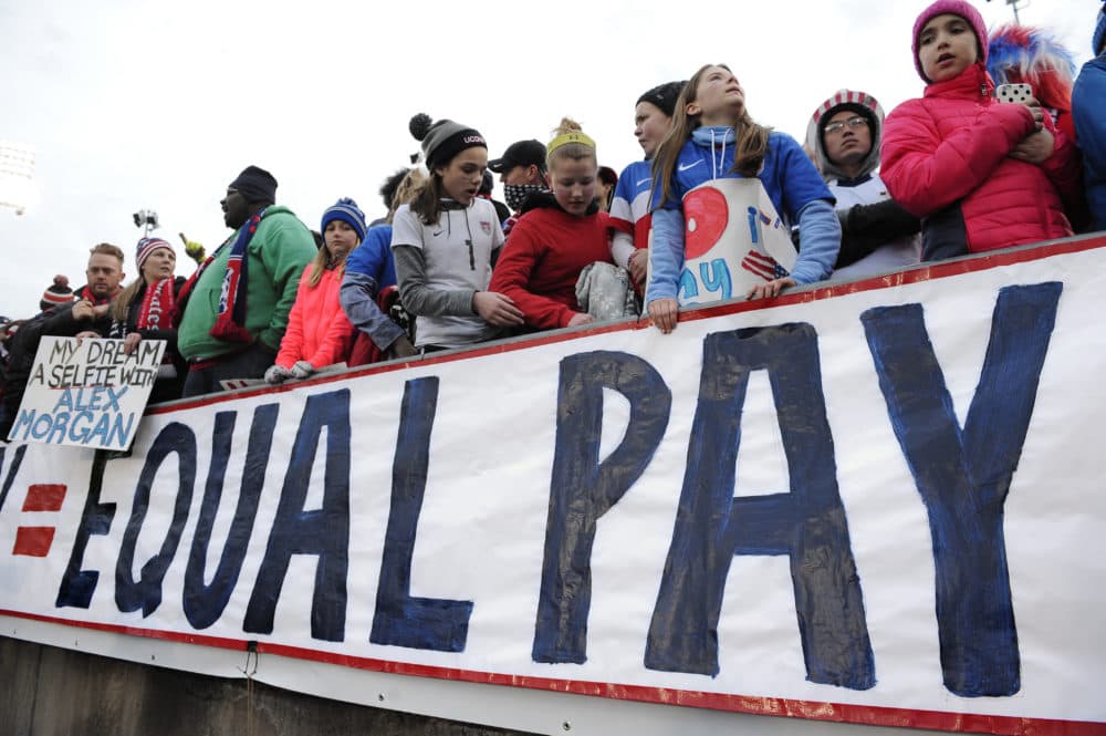 Fans stand behind a large sign for equal pay for the women's soccer team during an international friendly soccer match in 2016. (Jessica Hill/AP)