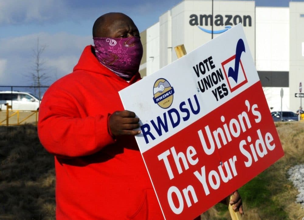 Michael Foster of the Retail, Wholesale and Department Store Union holds a sign outside an Amazon facility where labor is trying to organize workers on Tuesday, Feb. 9, 2021. (AP Photo/Jay Reeves, file)