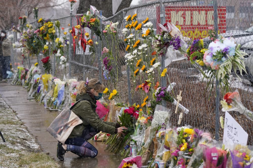 A mourner leaves a bouquet of flowers along a fence put up around the parking lot where a mass shooting took place in a King Soopers grocery store on Tuesday, March 23, 2021, in Boulder, Colo. (David Zalubowski/AP)
