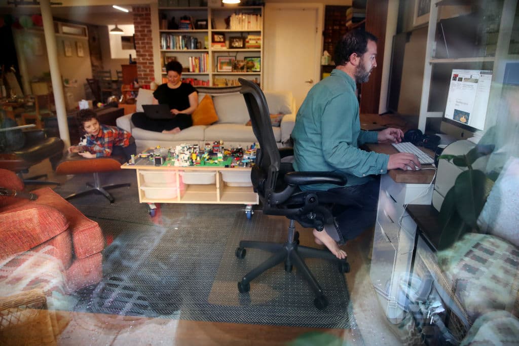 Seth, right, and Nicole Kroll work on their computers while their son Louis, 5, entertains himself at their home in Jamaica Plain on April 14, 2020. (Craig F. Walker/The Boston Globe via Getty Images)