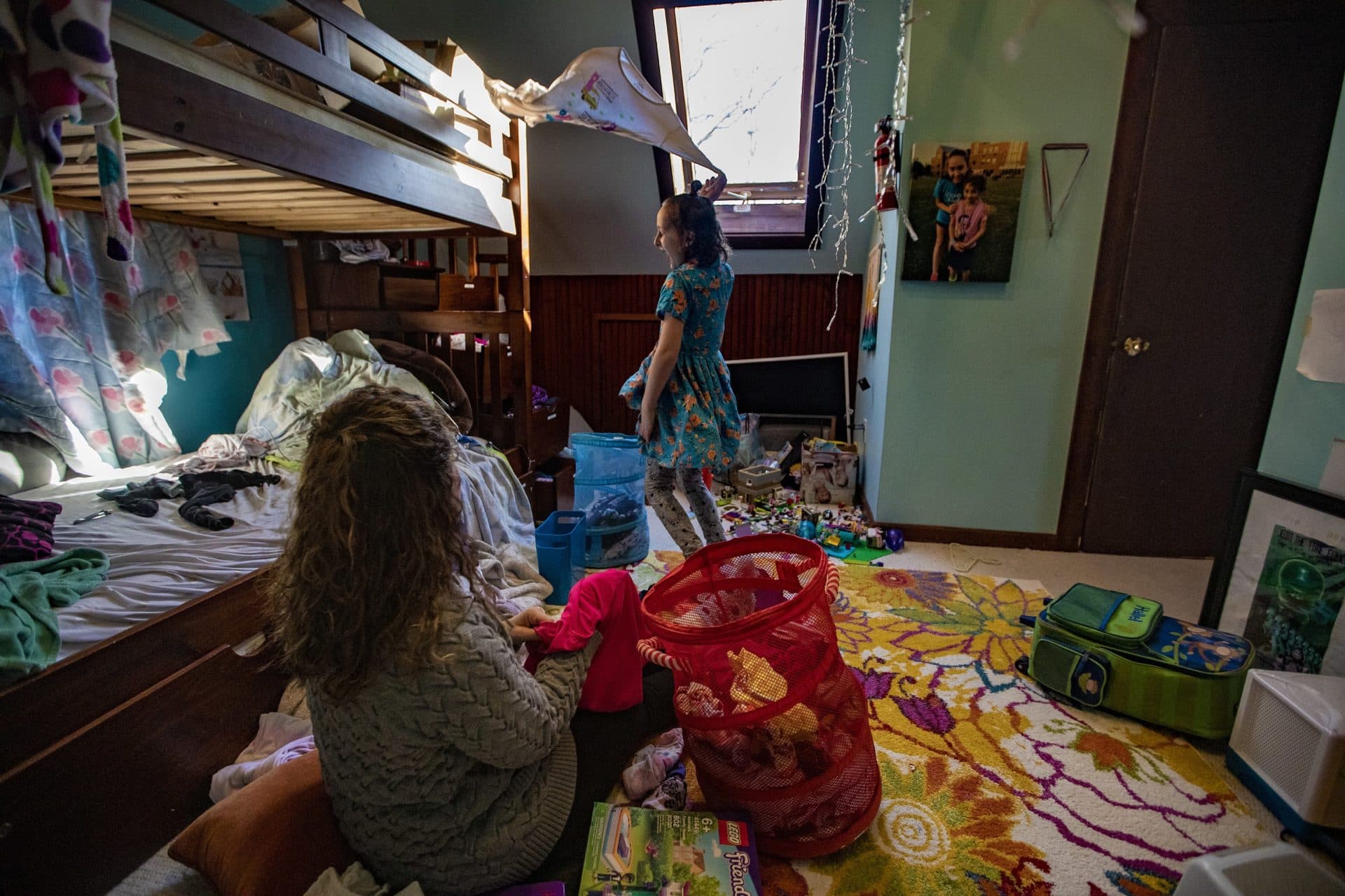 Hallel swings a T-shirt over their head while they and Shira organize clothes. (Jesse Costa/WBUR)