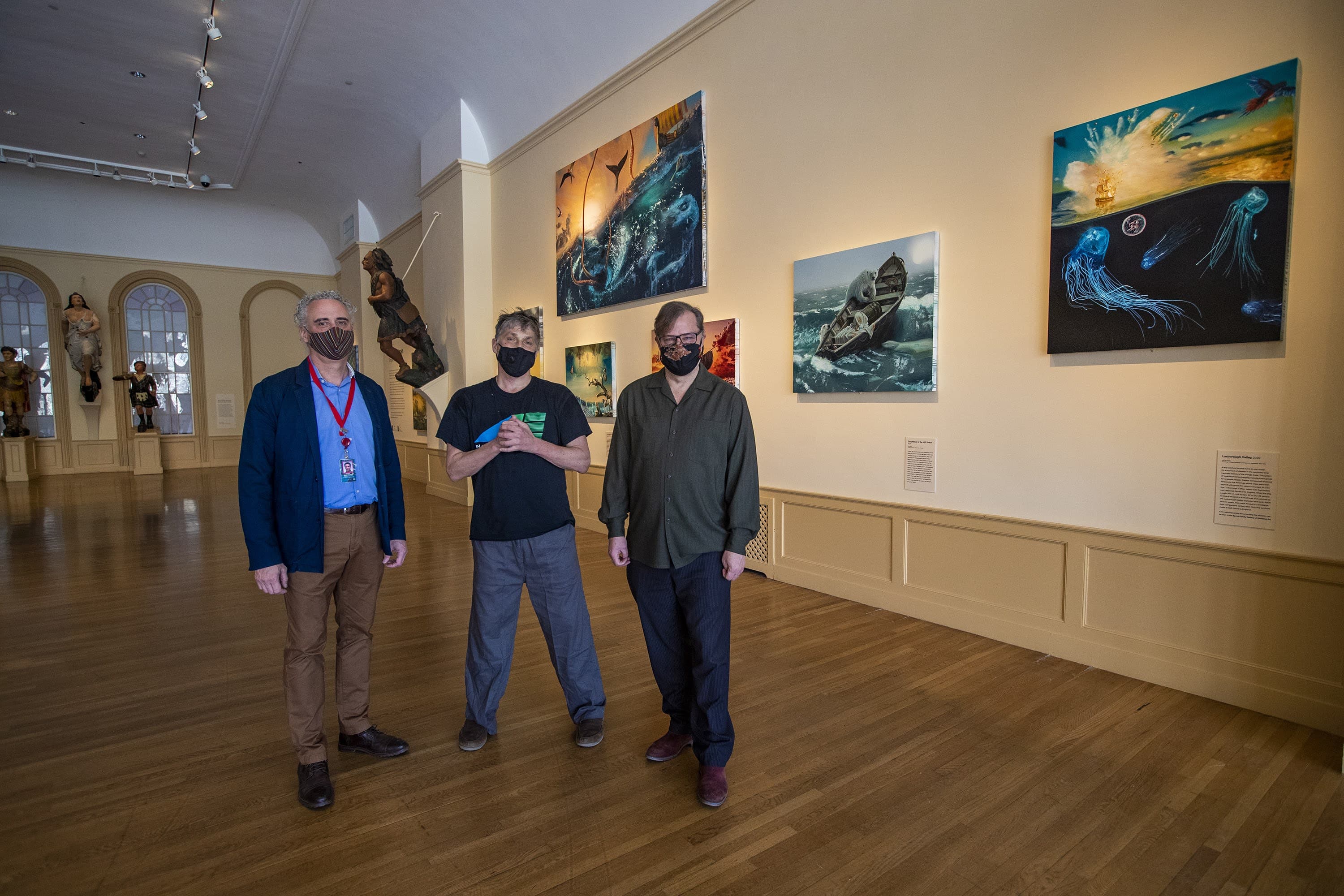 Daniel Finamore, Alexis Rockman, and Trevor Smith standing in front of Rockman’s paintings in the exhibit “Shipwrecks” in the East India Marine Hall at the Peabody Essex Museum. (Jesse Costa/WBUR)