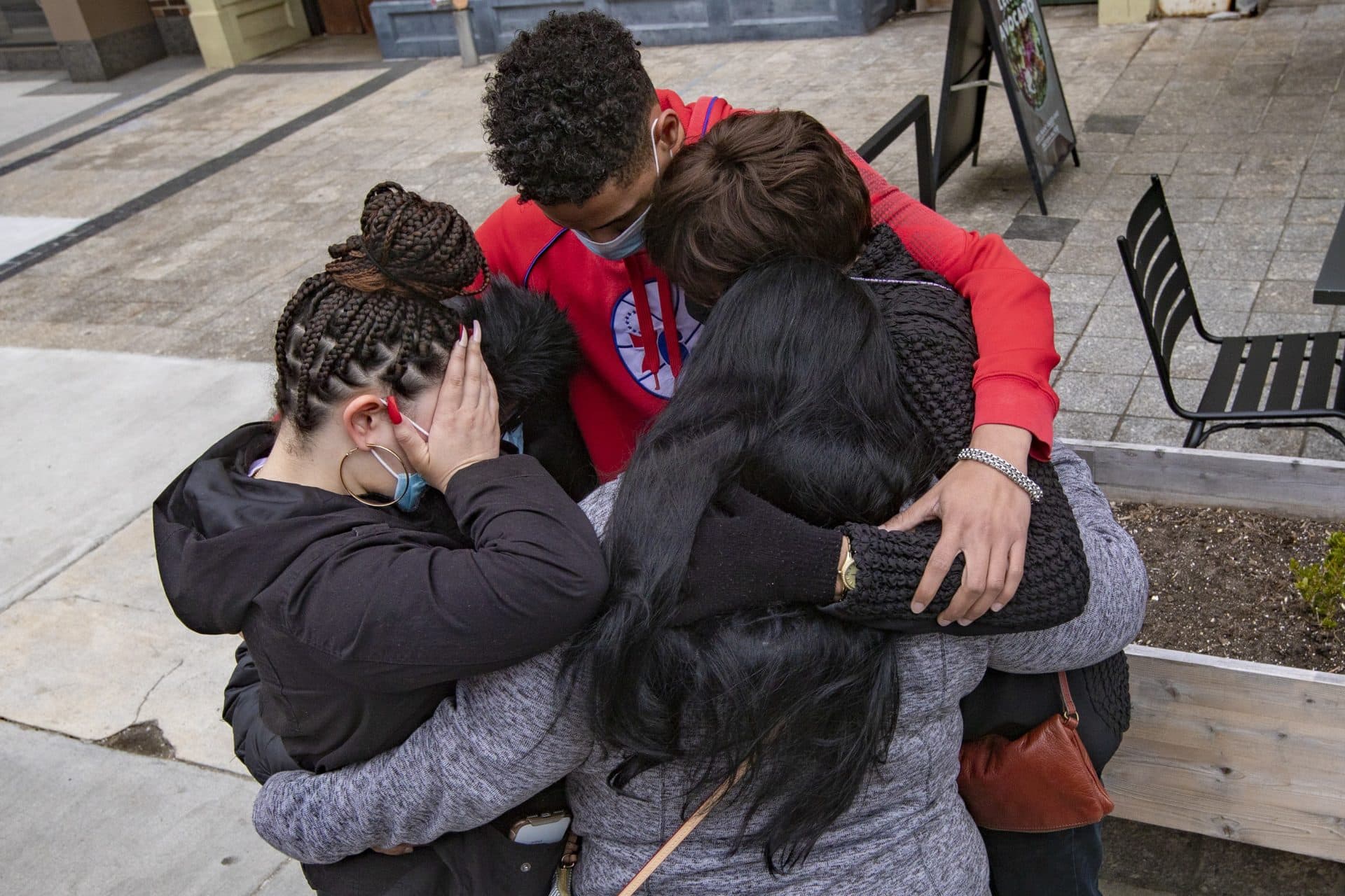 Boston Marathon bombing survivors Joselyn Perez, her mother Sara Valverde Perez and Laurie Scher, embrace with her brother Yoelin Perez and her aunt Susana Hunter during the moment of silence at the site of the finish line of the Boston Marathon on Boylston Street to mark the eighth anniversary of the bombing. (Jesse Costa/WBUR)